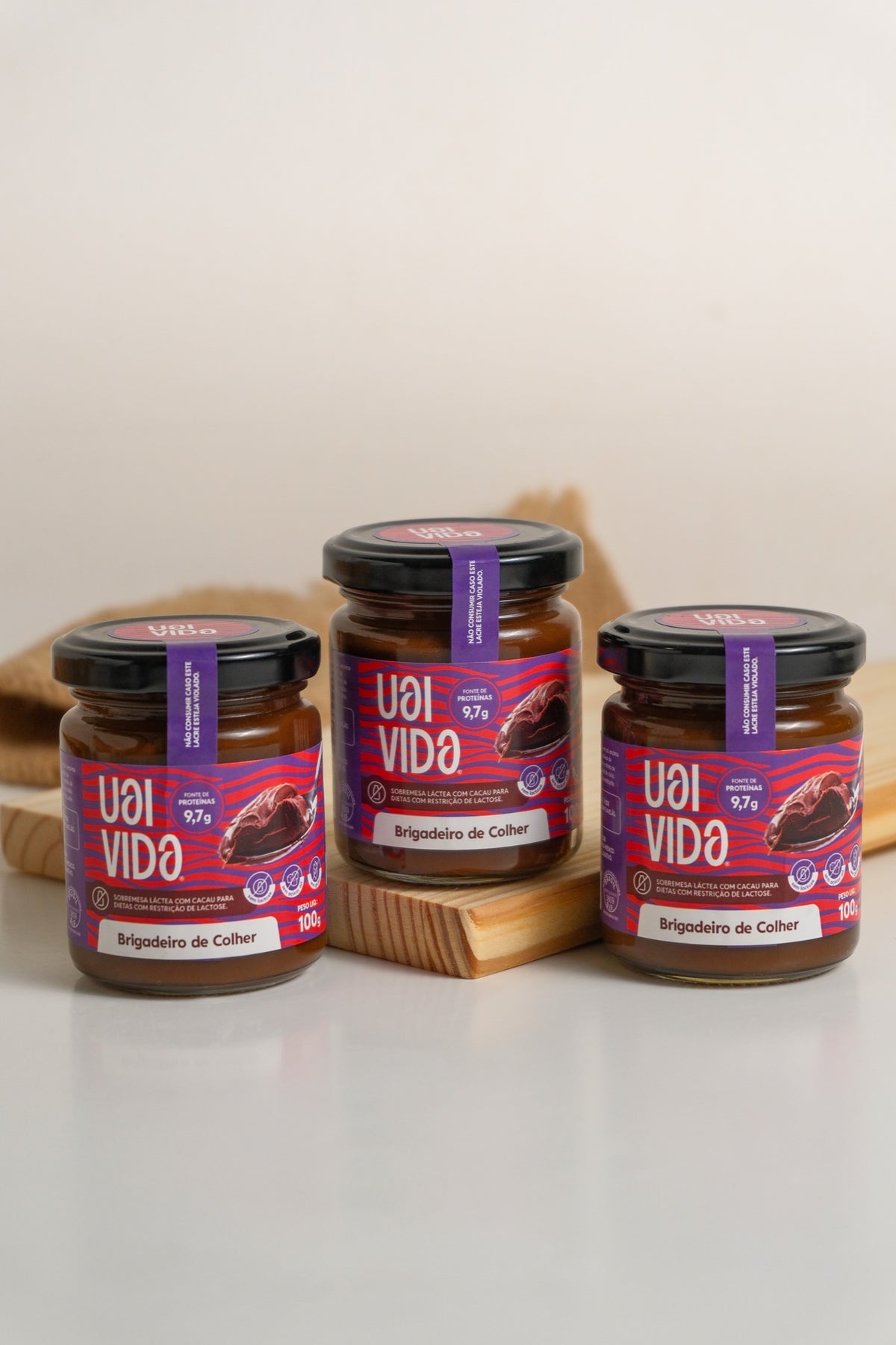 Três potes de Brigadeiro de Colher Uai Vida alinhados sobre tábua de madeira